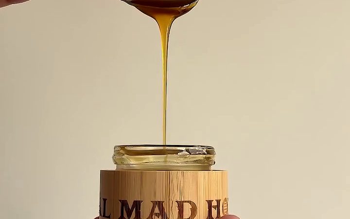 Honey running off a spoon into a bamboo jar of Real Mad Honey