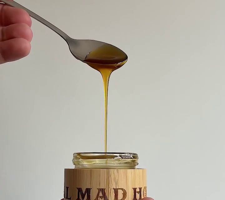 A teaspoon of dark honey dripping into a small bamboo jar