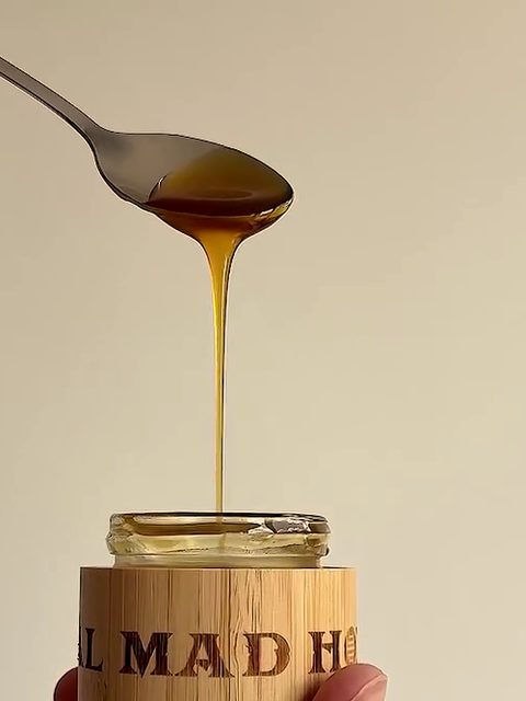 A spoon of dark honey dripping into a bamboo jar of Real Mad Honey